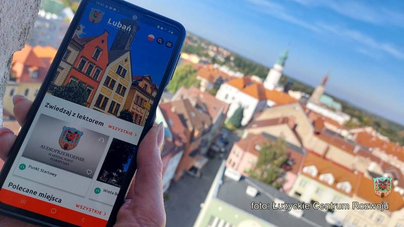 dłoń trzymająca telefon z aplikacją na tle panoramy miasta